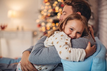 Father hugging daughter with christmas tree in the background