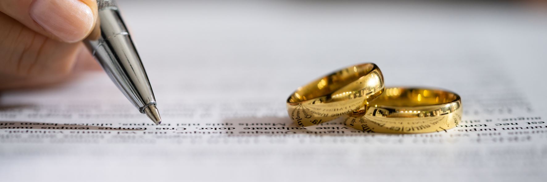 A close up shot of a pen on paper beside two stacked wedding rings.